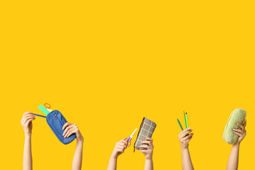 Female hands with pencil cases and stationery on yellow background