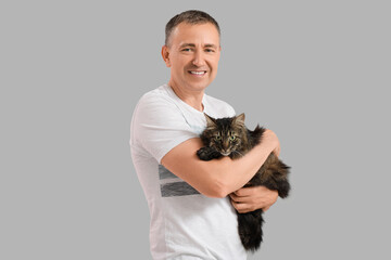 Mature man holding cute cat on grey background