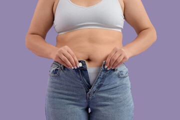 Overweight young woman in tight jeans on purple background, closeup. Weight gain concept