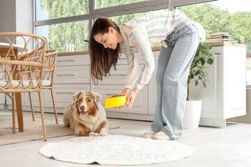 Young woman feeding Australian Shepherd dog with dry food at home