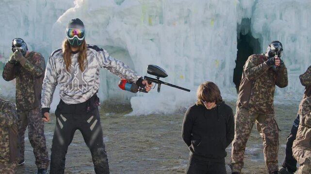 Masked person pointing paintball gun at hostage in icy area - slow motion