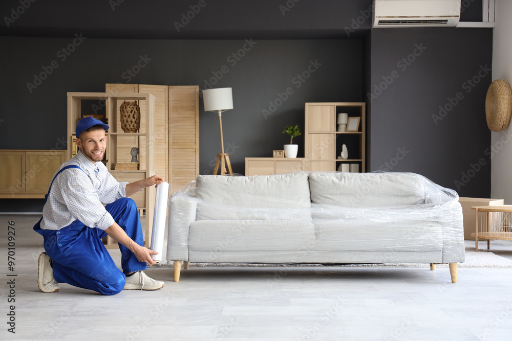 Sticker Male worker wrapping sofa with stretch film in room