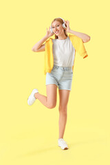 Young pretty woman in headphones listening music on yellow background