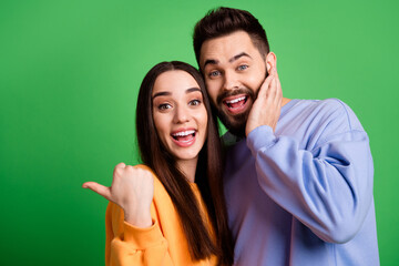 Photo of cheerful excited couple wear stylish sweatshirt recommend empty space isolated on green...