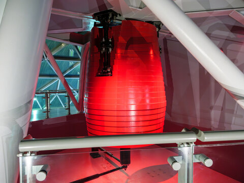 Red tuned mass damper pendulum is installed on the top floor of a high-rise structure, designed to reduce the building's oscillations during high winds or seismic activity and ensure stability.