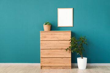 Chest of drawers, houseplant and frame  near blue wall in room
