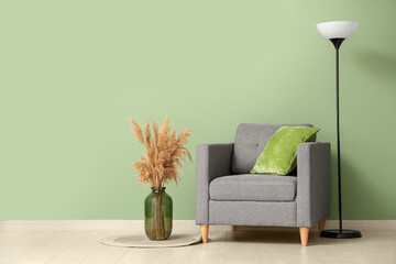 Armchair, pampas grass in vase and floor lamp near green wall in room