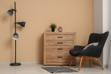 Chest of drawers, armchair and floor lamp near beige wall in room