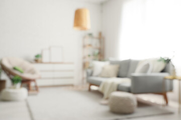 Comfortable sofa, chest of drawers, armchair and pouf in interior of living room. Blurred view