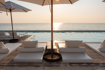 swimming pool on sea view and umbrella and chair in hotel resort with sunset