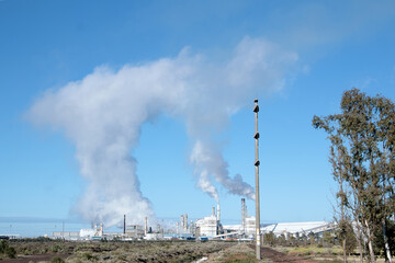 Factory emitting large amounts of smoke into the blue sky, causing air pollution and contributing...