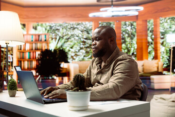 Entrepreneur using his laptop to manage business activities and financial planning, ensuring successful remote work. Developing budget and project details from his home office setup.