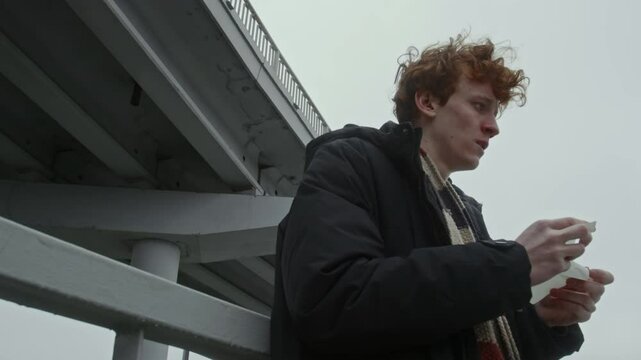 View from below of distraught young man looking at piece of paper, turning around, grabbing railing and squeezing note outdoors