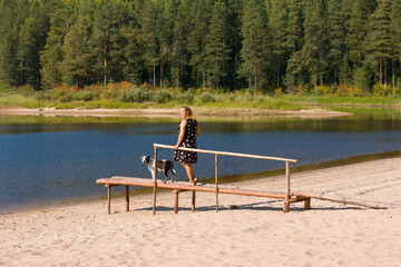 A woman in a sundress on an empty beach with a cup of coffee. A barefoot woman stands with her back to him