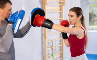 Young woman in punch gloves training with coach in gym