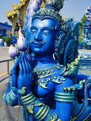 Fototapeta premium This vibrant close-up captures a blue deity sculpture at Wat Rong Suea Ten, the Blue Temple, in Chiang Rai, Thailand. The figure is adorned with intricate details and golden highlights.