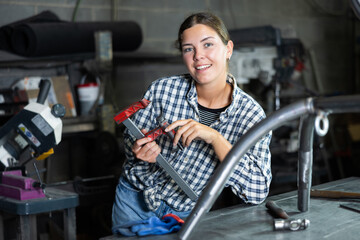 Young female worker in uniform posing with vice in metallurgical workshop