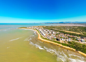 Imagem aérea da praia de Castelhanos em Anchieta, em uma manhã ensolarada. Praia deserta, ondas do mar e barracas na areia.