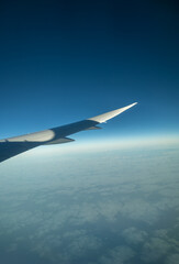 Close-up of aircraft wing flying over sea of clouds with blue sky. Concept: Journey, travel, holiday.