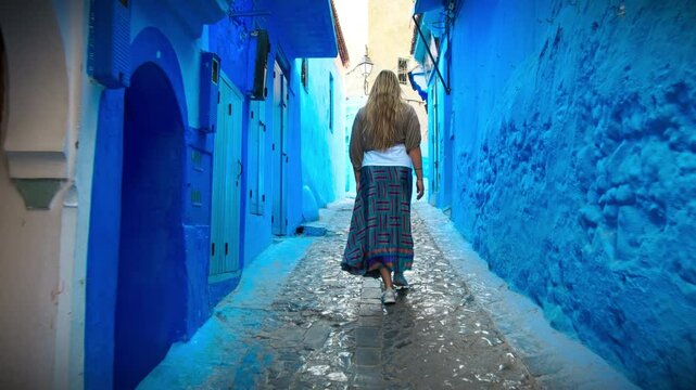 European blonde girl walking in Medina alleys and stairs of Chefchaouen, the famous Blue Pearl of Morocco or Blue City. Chaouen is noted for its buildings in shades of blue, UNESCO heritage.