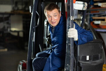 Adult male worker in uniform posing while sitting in forklift in metallurgical workshop