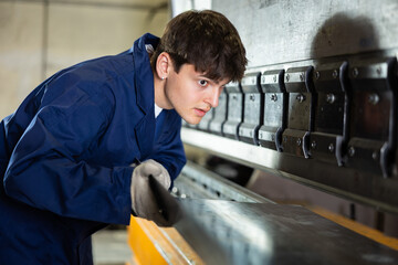 Young worker works on sheet bending machine at a metallurgical plant