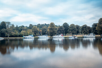 Obraz premium A row of boats docked on a calm river with a cloudy sky.