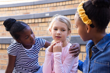 Comforting friend, two multiracial schoolgirls supporting another girl during break time
