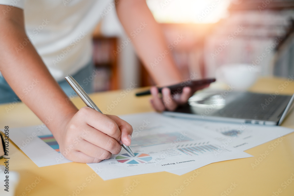 Poster close-up of a person analyzing financial data with charts and graphs, using a pen and smartphone, in