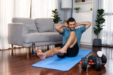 Athletic and sporty man doing crunch on fitness mat during home body workout exercise session for fit physique and healthy sport lifestyle at home. Gaiety home exercise workout training concept.
