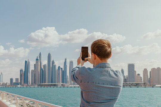 Young man taking selfie by the waterfront on his smartphone with a city skyline on the background