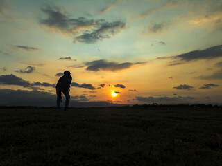 Fototapeta premium Silhouette of a man standing in a meadow at sunset. Nature and beauty concept. Silhouette at sunset, panoramic photo.