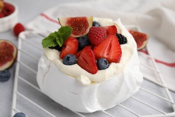 Pavlova cake (meringue dessert) with whipped cream, fresh berries, mint and fig on light grey table, closeup