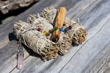 A close up image of white sage smudge sticks with a rose quartz crystal pendulum.