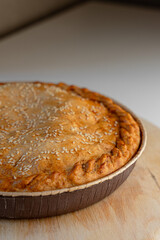 Pie with a golden crust and sesame seeds, resting on a wooden stand.