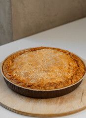 Pie with a golden crust and sesame seeds, resting on a wooden stand.