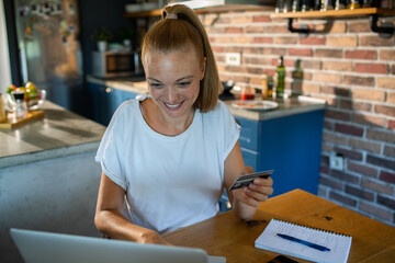 Young woman shopping online with credit card at home kitchen