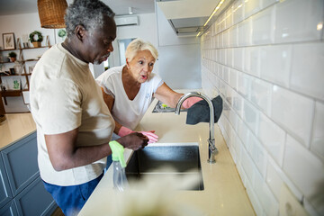 Obraz premium Diverse senior couple cleaning kitchen together