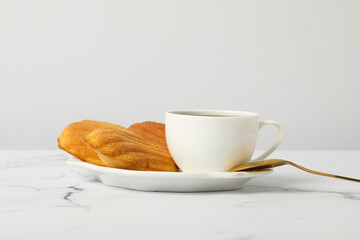 Madeleine cakes, cup of coffee and spoon on marble background, close up