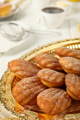 Madeleine cakes on golden dish, flour and cup on light background, close up