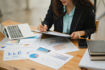 Businesswoman Analyzing Data: A focused businesswoman meticulously reviews financial reports, surrounded by graphs and charts. The image captures her dedication and commitment to strategic decision-ma