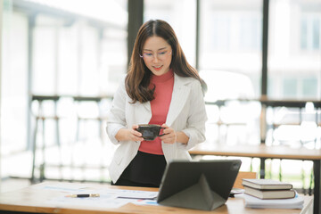 Focused Elegance: Young Asian professional woman in stylish office attire reviews financial reports at her modern workspace.