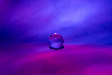 Glass ball with shades of blue and pink, cloud-like background.