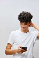 Portrait of a young man with curly hair looking at his smartphone against a light gray background,...