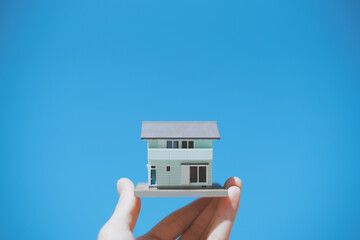 住宅模型を持つ人の手と青空背景