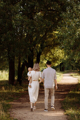 Fototapeta premium A family of three, a man and a woman with a child in their arms, stand in a park in the summer. The concept of a happy family with a small child, care and love.