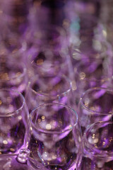 A bunch of glasses are lined up on a table. The glasses are purple and have a blurry background