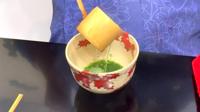 Preparation of Matcha involves woman whisking ground green tea powder into frothy, bright drink. Rooted in Japanese tradition, tea-making ritual focuses on mindfulness and connection to natur