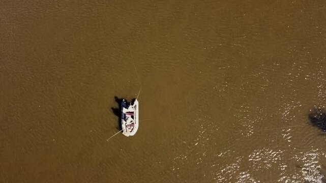 A boat is floating on a brown body of water. The boat is small and has a person in it. The water is murky and the boat is the only thing visible in the image