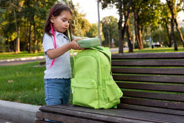Little girl organizing backpack on park bench in afternoon light